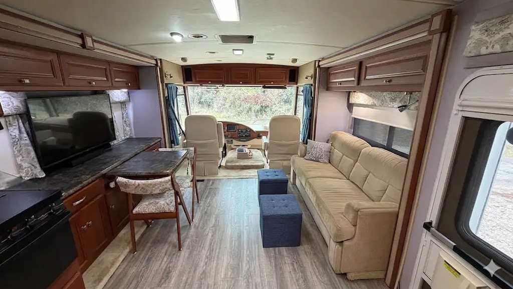 Clean, modern interior of a 2013 Winnebago Itasca Sunstar 30T Class A motorhome showing the spacious kitchen, living area, and upgraded wood-look laminate flooring with slides extended.